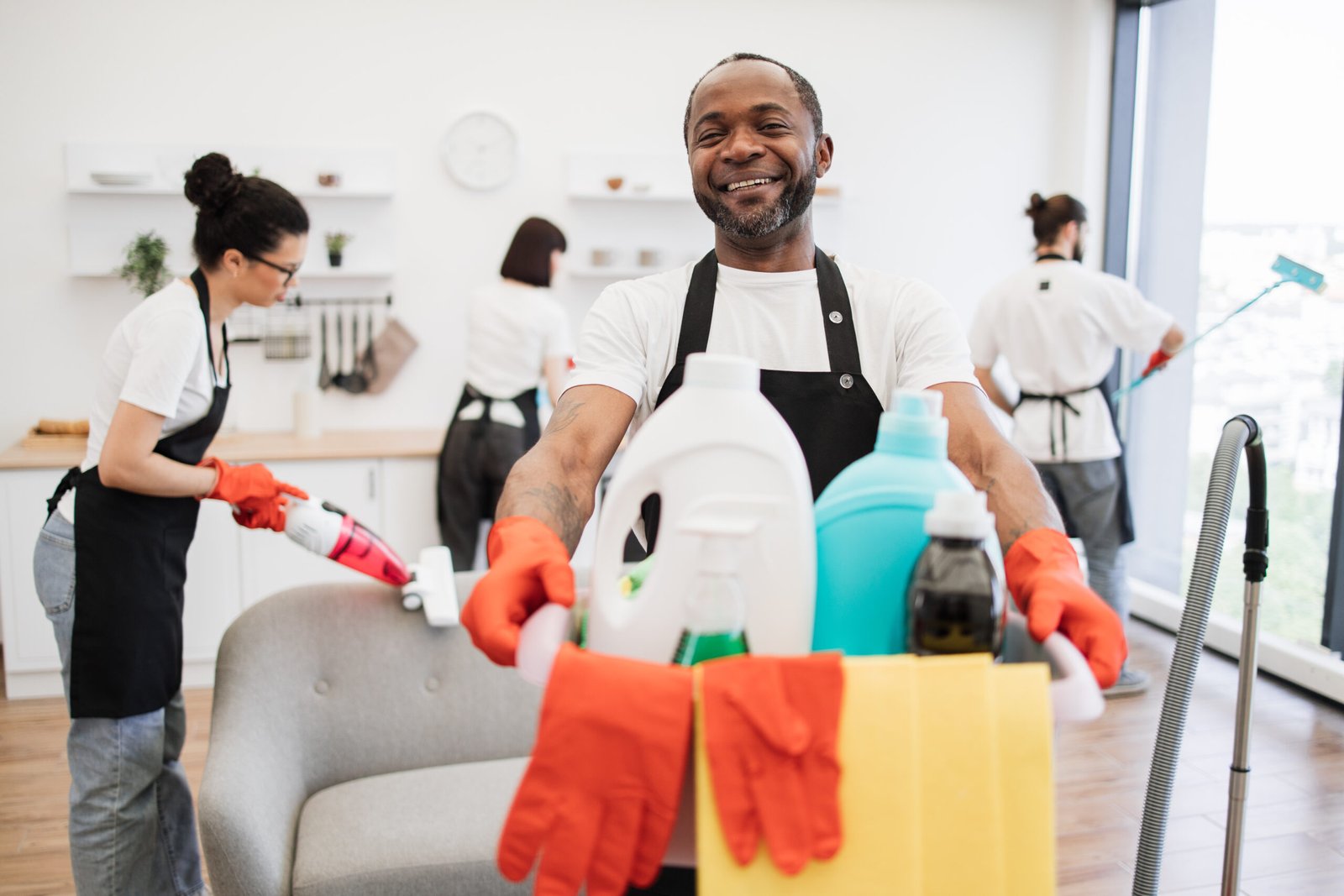 Portrait of young African American man professional cleaning worker holding a bucket for washing with detergents on bright kitchen studio background, copy space.